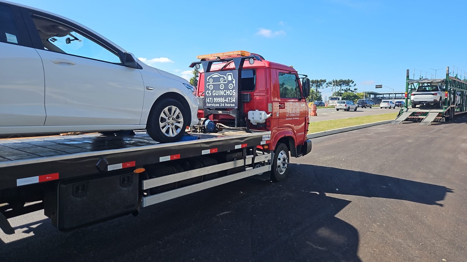 Caminhão plataforma vermelho da CS Transportadora transportando um carro em dia claro